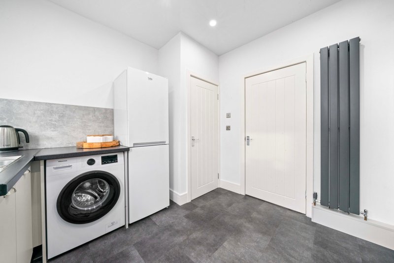 Modern utility room with white washing machine, fridge, and gray radiator