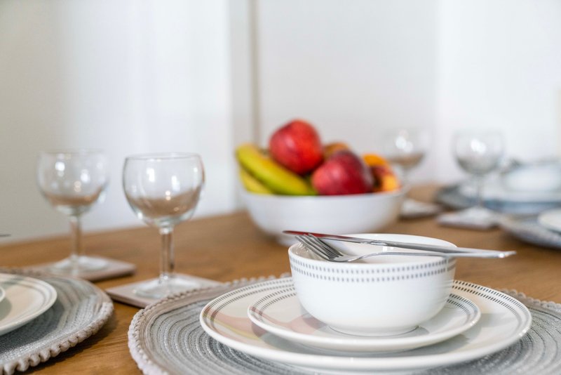 Dining table set with plates, bowls, glasses and fruit bowl in background