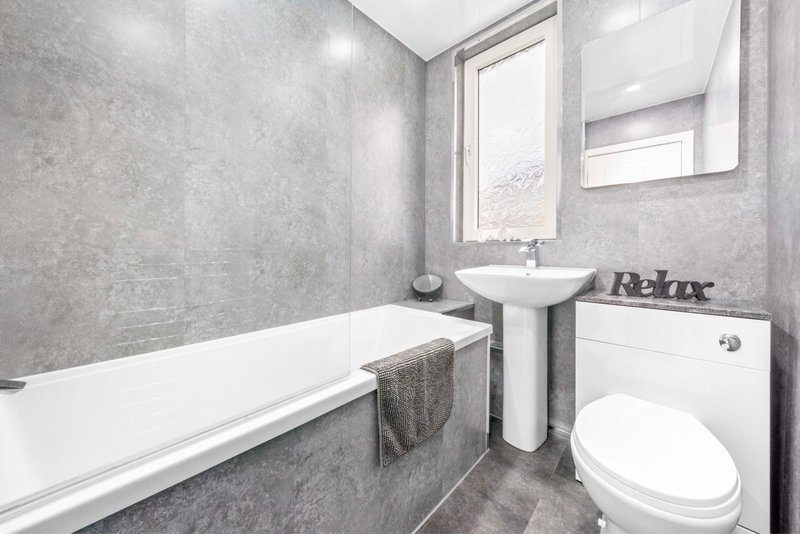 Modern bathroom with bathtub, pedestal sink, toilet, and window with natural light