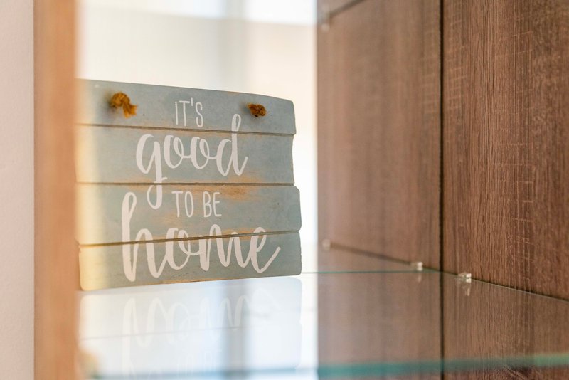 Entryway with wooden wall-mounted sign reading 'it's good to be home' and glass door