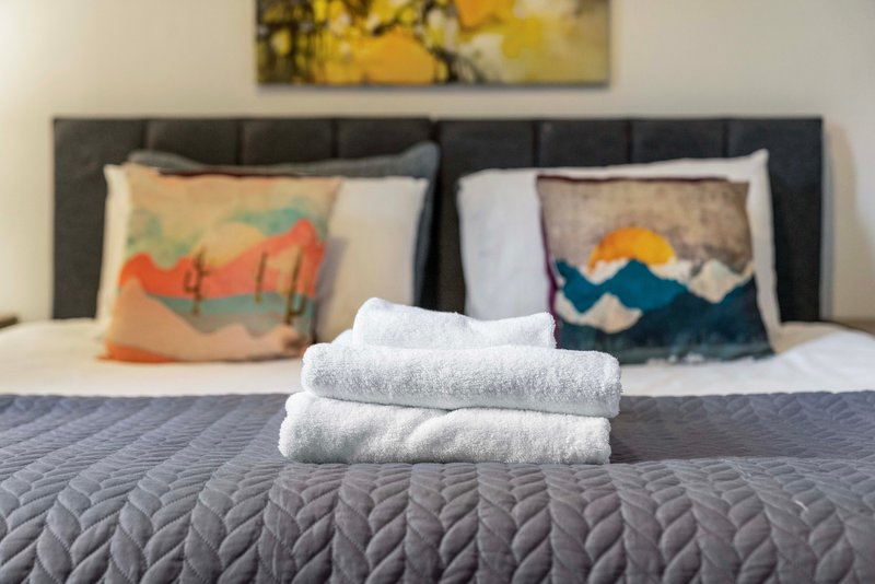 Bedroom with dark headboard, folded white towels on bed, decorative pillows, and wall art