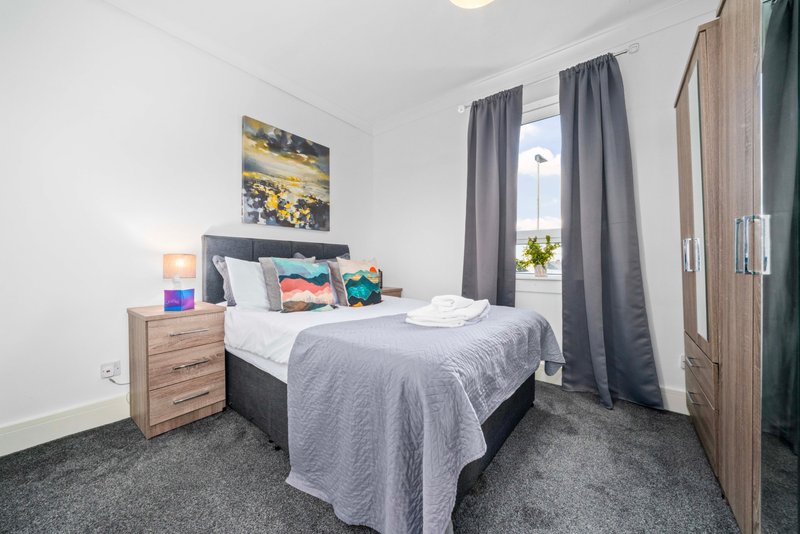 Modern bedroom with double bed, grey bedding, wooden nightstand, wall art and grey curtains