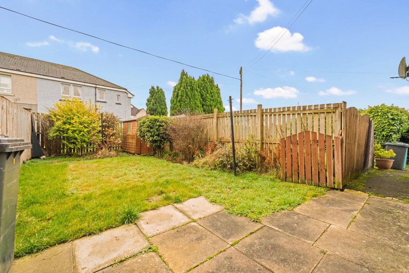 Residential garden with paved patio, lawn, wooden fence and mature shrubs