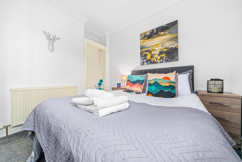 Bright modern bedroom with double bed, colorful cushions, wooden furniture and wall art