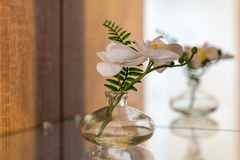 Glass vase with white flowers and green foliage on wooden shelf