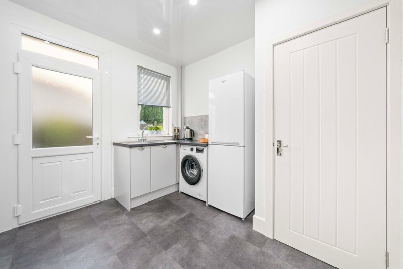 Modern utility room with washing machine, white cabinetry, and grey tiled floor