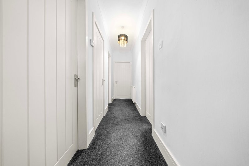 Long hallway with white panelled walls, dark grey carpet and ceiling light fixture