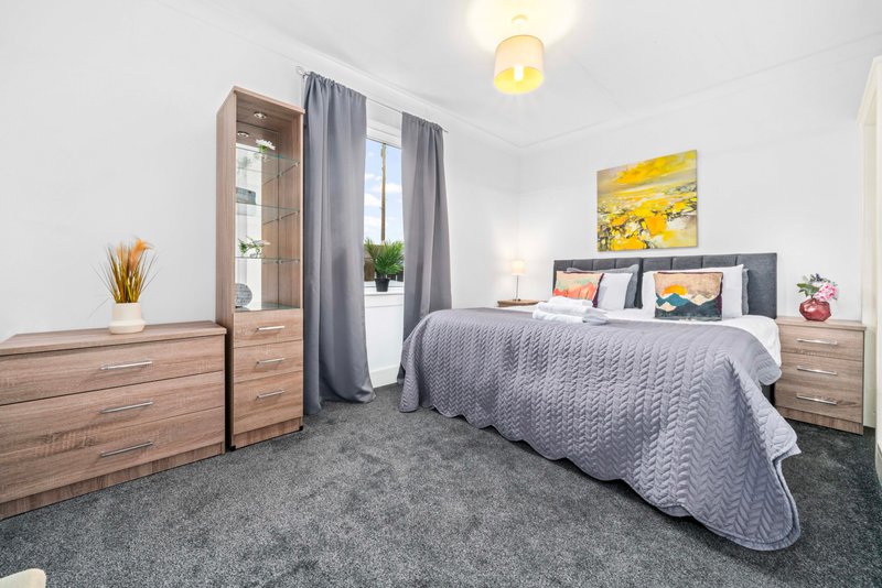 Bright modern bedroom with double bed, wooden furniture, grey carpet and window with curtains
