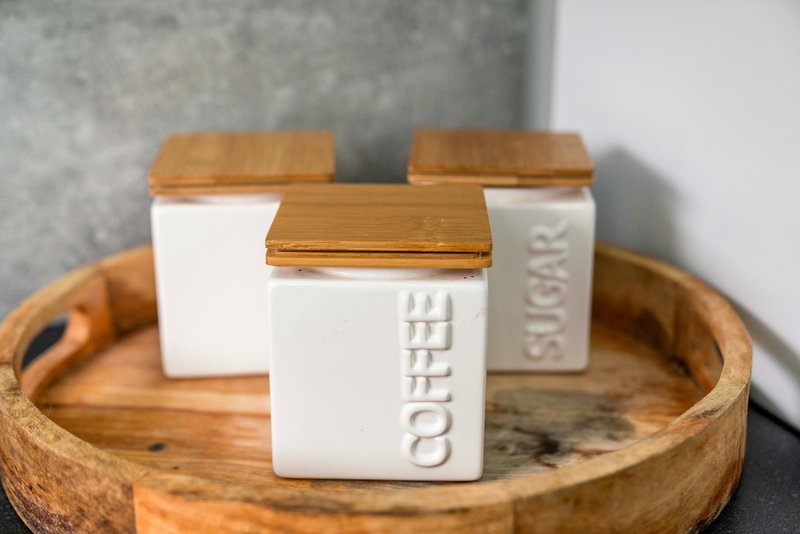 Wooden tray with three white ceramic containers with wooden lids, one labeled coffee