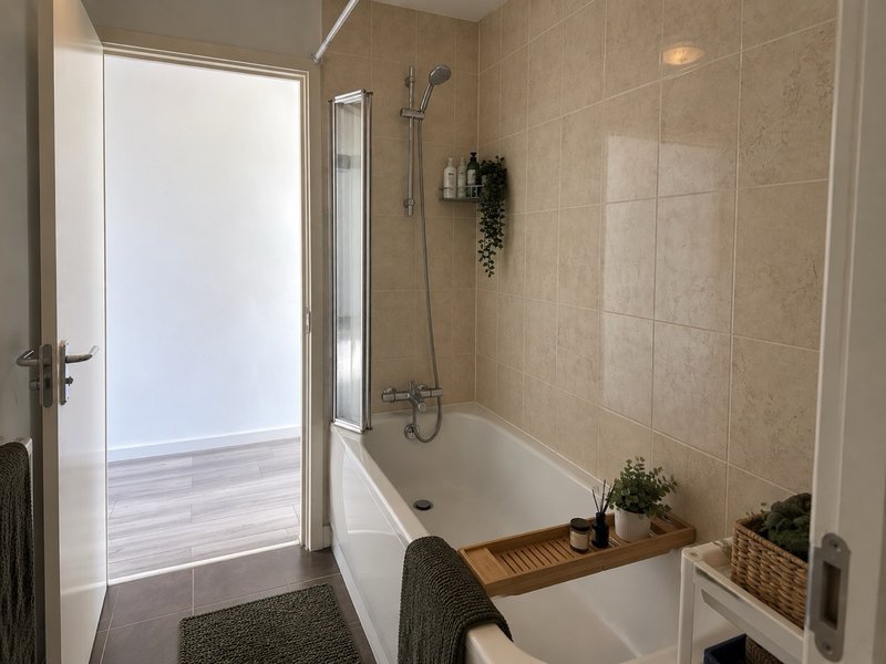 Modern bathroom with white bathtub, glass shower screen, beige tile walls and potted plants