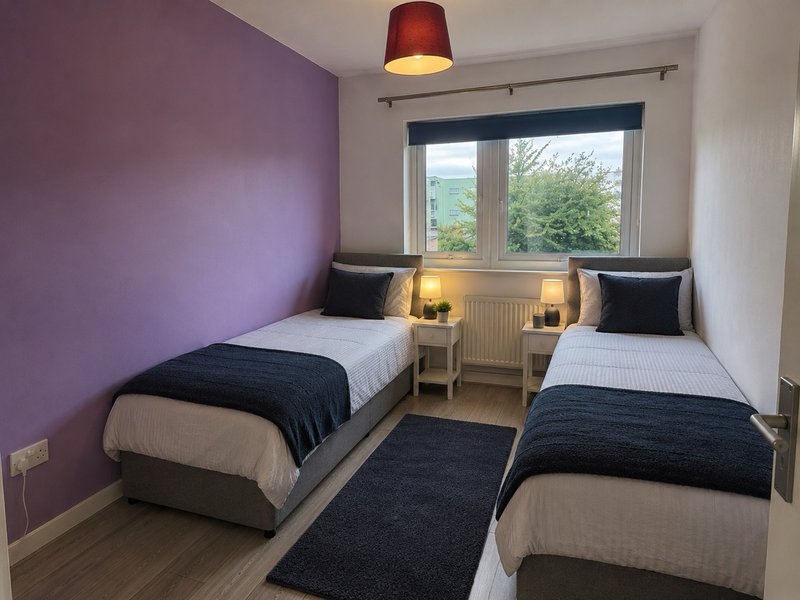 Twin bedroom with purple accent wall, two single beds, bedside lamps and window view
