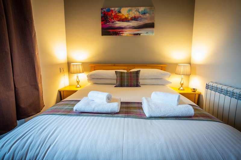 Bedroom with double bed, white towels, bedside lamps, and landscape artwork above headboard