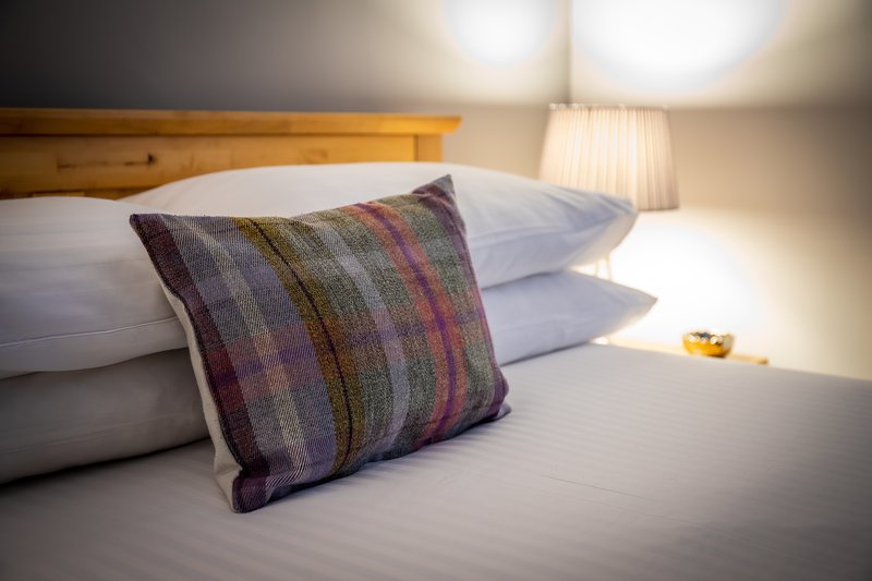Bedroom with wooden headboard, white pillows, striped cushion, and bedside lamp