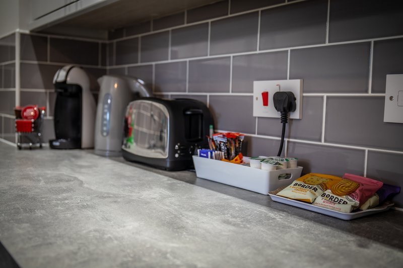 Kitchen counter with coffee makers, kettle, and groceries on gray tiled backsplash