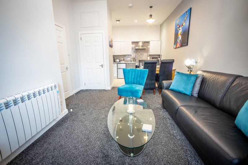 Modern living room with black leather sofa, blue accent chairs, glass coffee table and kitchenette