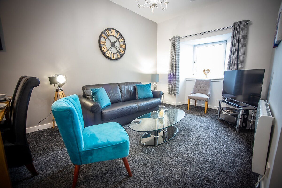Modern living room with turquoise armchair, dark sofa, glass coffee table and television