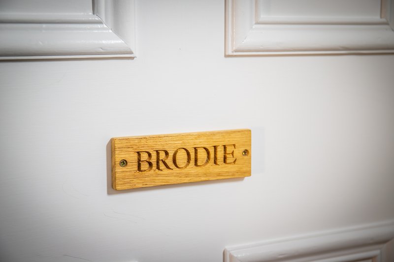 Wooden door nameplate reading 'BRODIE' mounted on white panelled wall