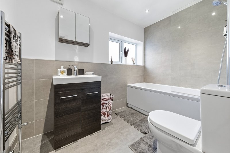 Modern bathroom with dark vanity, white sink, bathtub and toilet, tiled walls