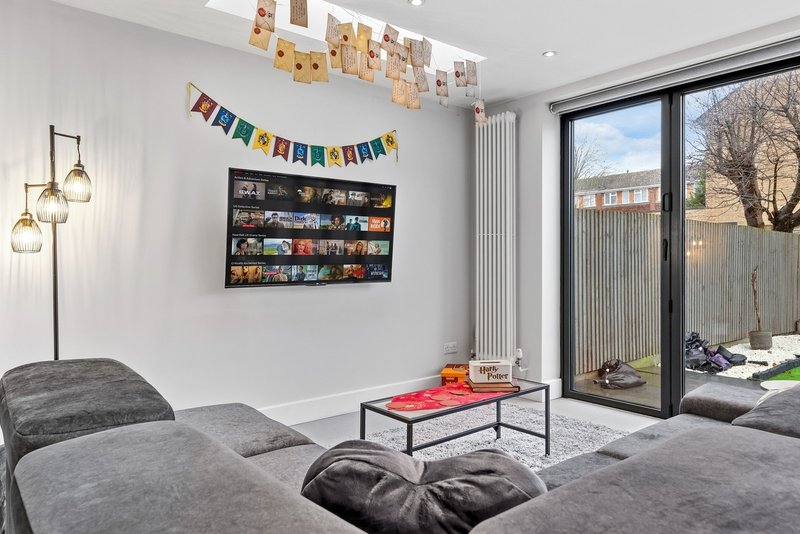 Modern living room with grey sofa, coffee table, wall shelving, and garden view through glass doors