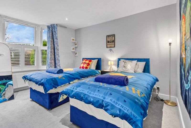 Bright twin bedroom with blue bedding, windows, wall art, and floor lamp