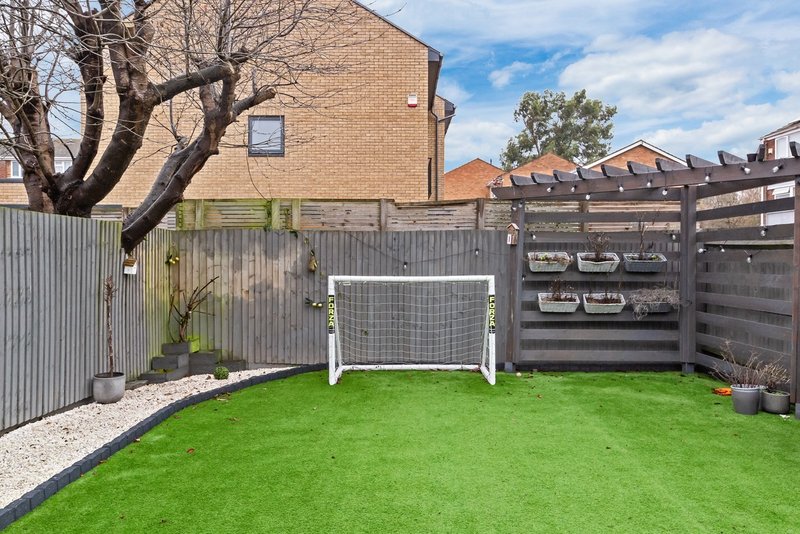 Outdoor garden with artificial grass, white soccer goal, wooden fencing and brick building