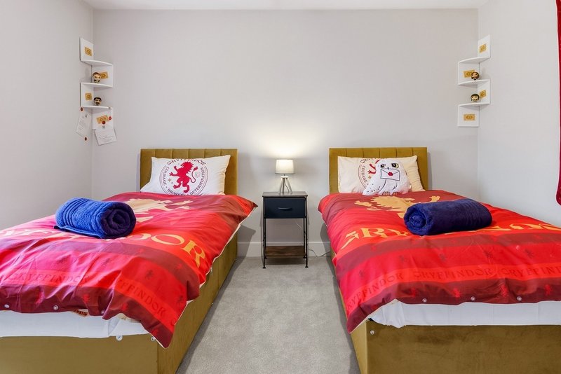 Twin bedroom with two single beds, red bedding, blue pillows, wooden frames, and wall shelving