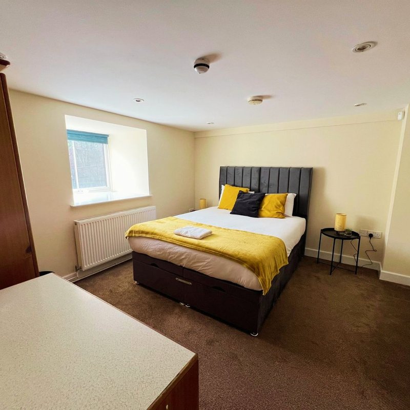 Bright bedroom with double bed, yellow bedding, gray headboard, window, and side table