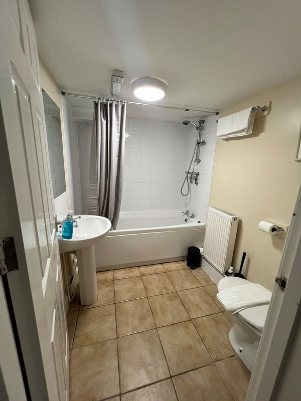 Bathroom with toilet, pedestal sink, bathtub with shower enclosure and tiled floor