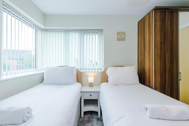 Twin bedroom with white bedding, wooden wardrobe, bedside table, and window with vertical blinds