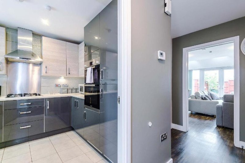 Modern kitchen with dark cabinetry, stainless steel appliances, and open doorway to living area