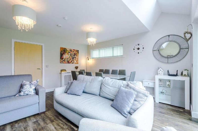 Bright open-plan living room with white sofa, grey armchair, wall art and decorative clock