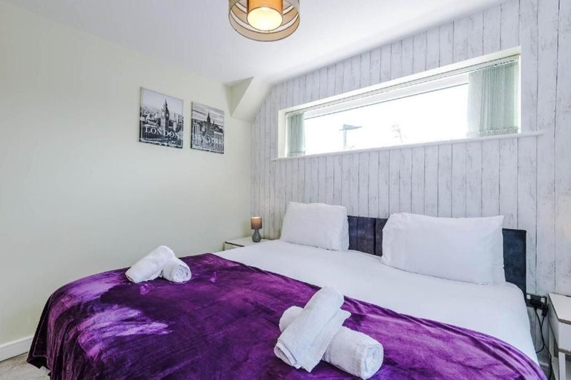 Modern bedroom with double bed, purple bedding, white pillows and window above headboard
