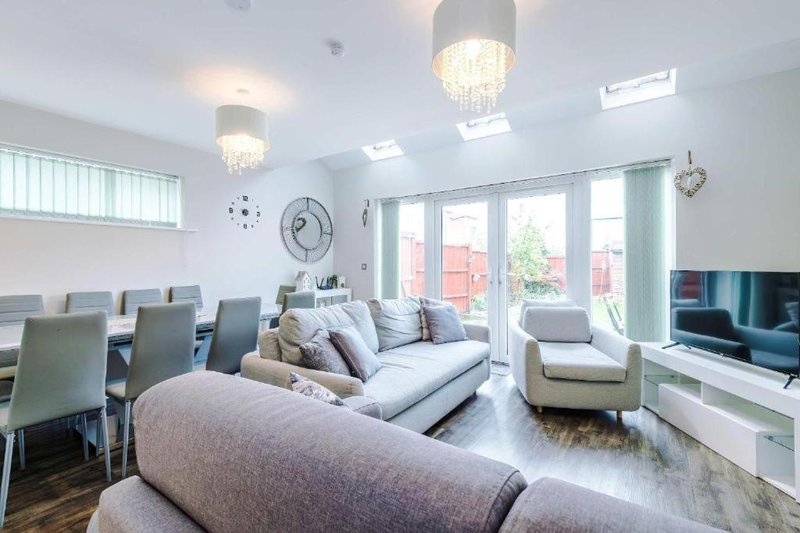 Modern open-plan living room with sofa, dining chairs, TV, and patio doors overlooking garden