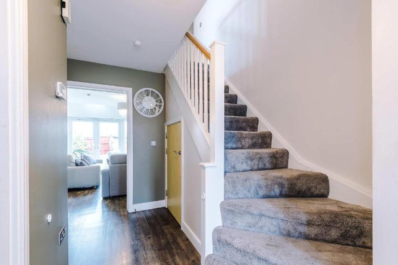 Hallway with staircase, wall clock, wooden flooring and door to living area