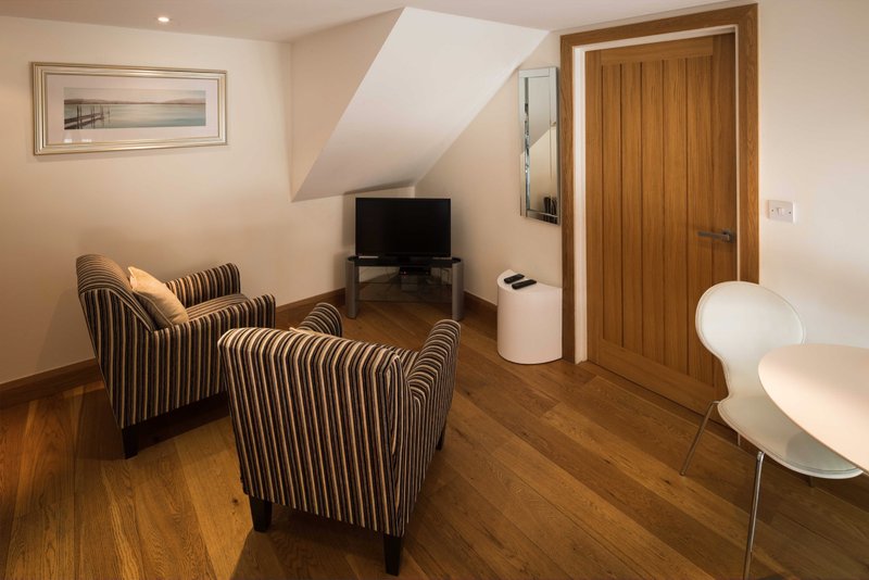Attic sitting room with striped armchairs, TV, wooden door and sloped ceiling