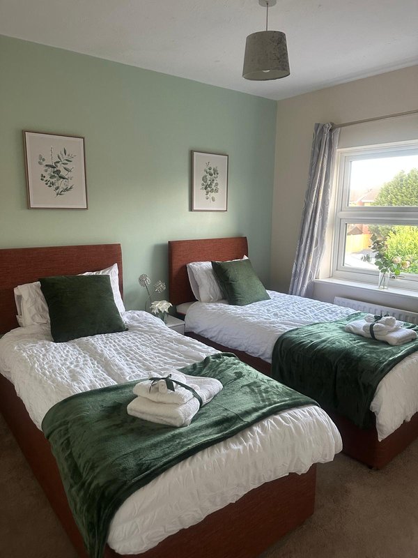 Twin bedroom with green walls, wooden bed frames, white bedding and green throws
