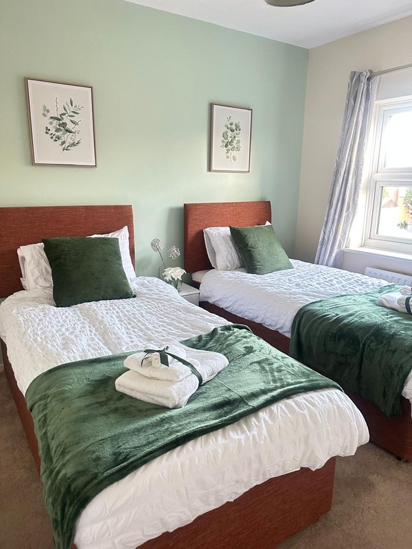Twin bedroom with green and white bedding, wooden headboards, botanical wall art and window
