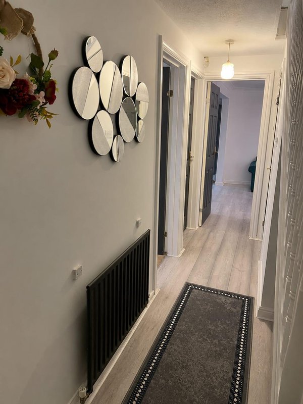 Hallway with decorative mirrors, black radiator, wooden flooring and runner mat