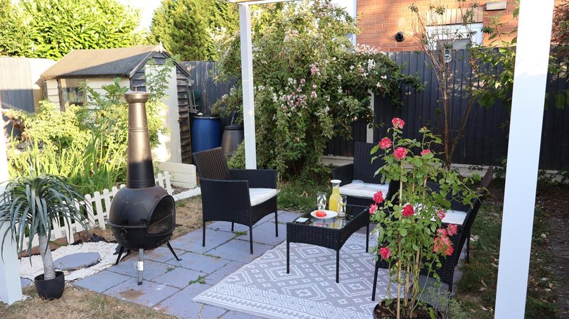 Garden patio with black chimenea, furniture, plants and flowering climbers