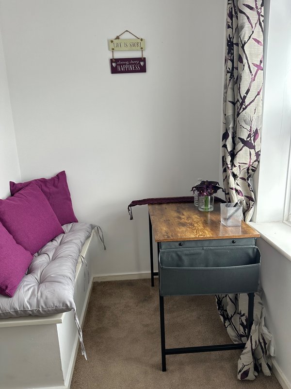 Small bedroom with purple cushioned window seat, wooden desk, and patterned curtains