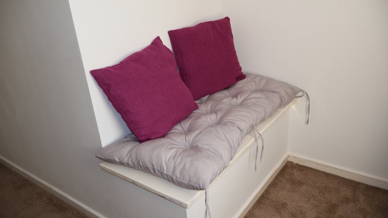 White built-in bench seat with grey cushion and two purple pillows
