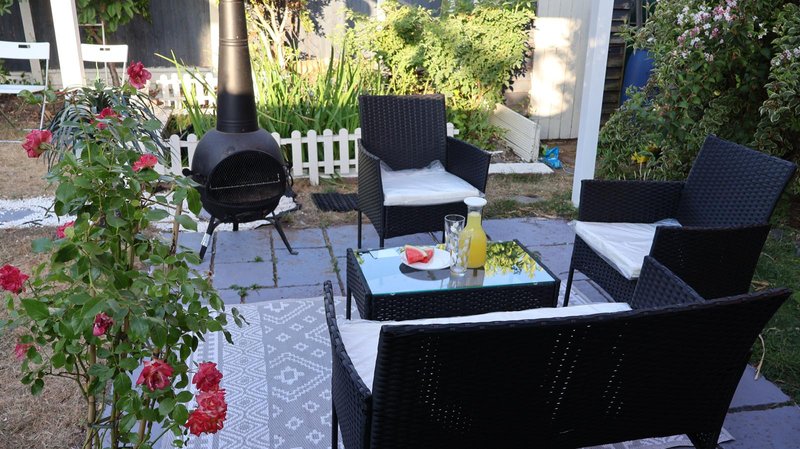 Outdoor patio with black wicker furniture, table, flowering plants and garden backdrop
