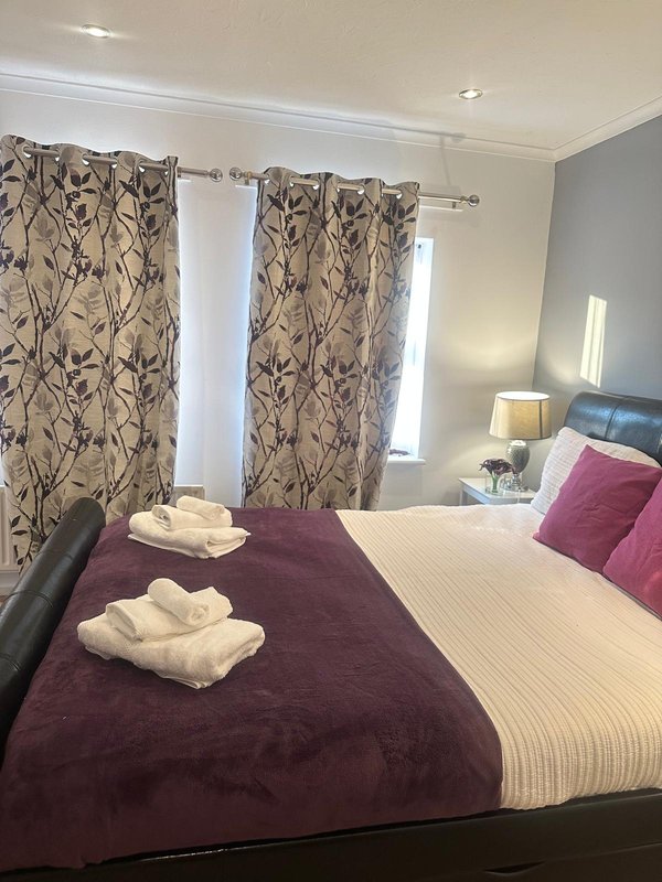 Bright bedroom with double bed, burgundy bedding, patterned curtains and bedside lamps