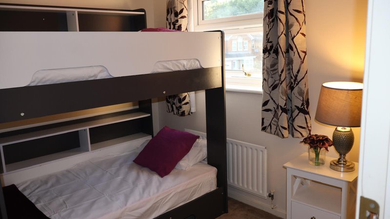 Bedroom with black bunk beds, burgundy cushion, window with patterned curtains, bedside lamp