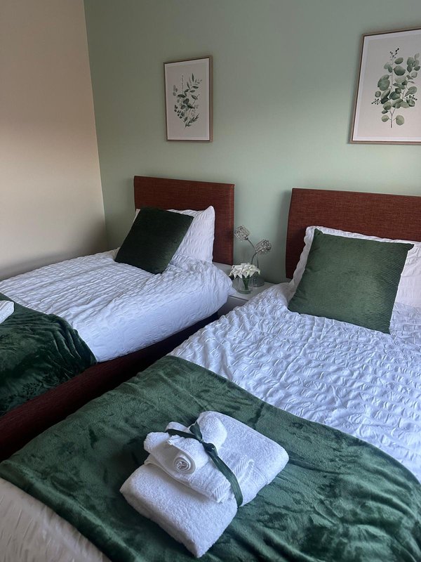 Twin bedroom with dark wood headboards, white bedding, green cushions and botanical wall art