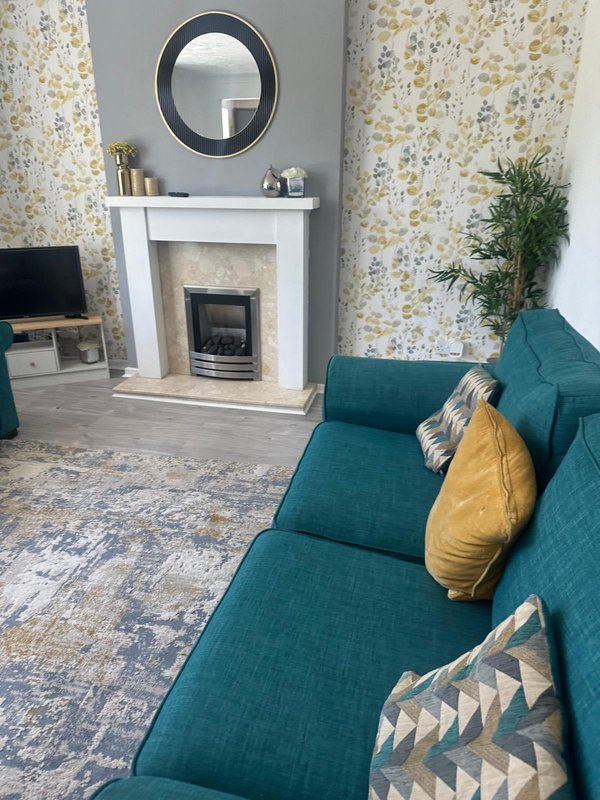 Living room with teal sofa, fireplace, round mirror, and patterned wallpaper