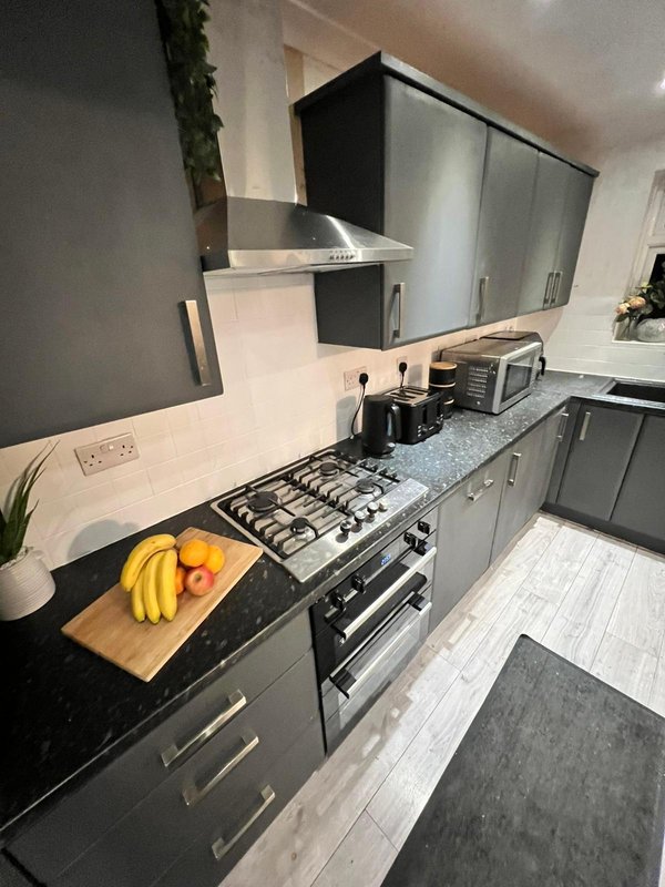 Modern kitchen with black cabinetry, gas range, white splashback and granite countertop