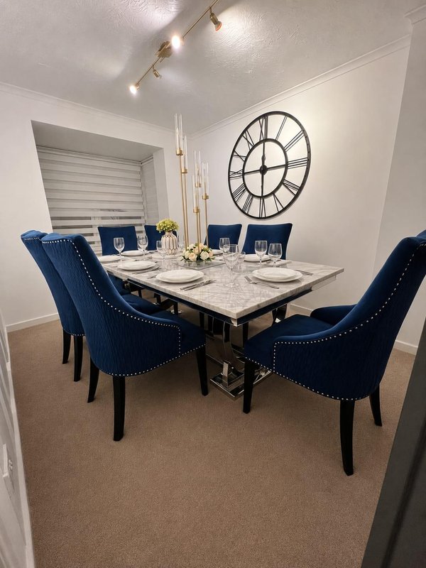 Dining room with marble table, blue upholstered chairs, large wall clock and track lighting