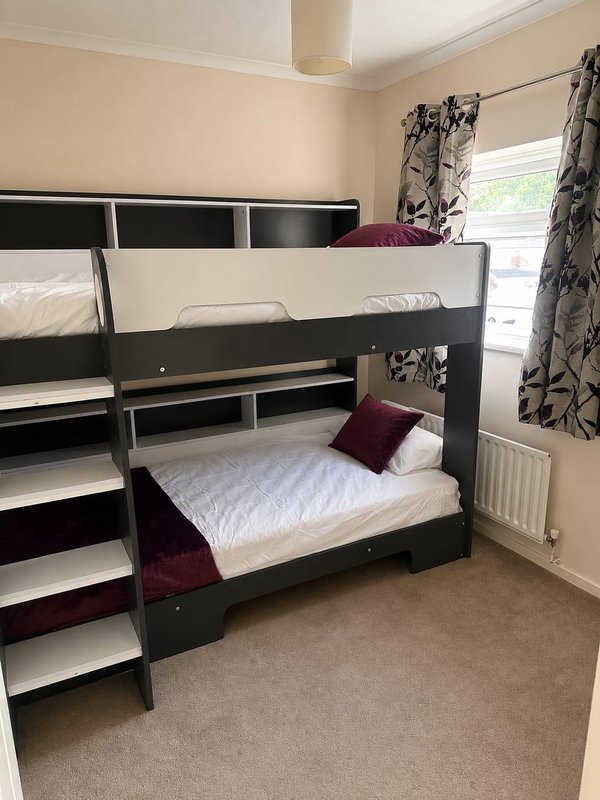Bedroom with black bunk beds, white mattresses, burgundy cushion, patterned curtains and radiator