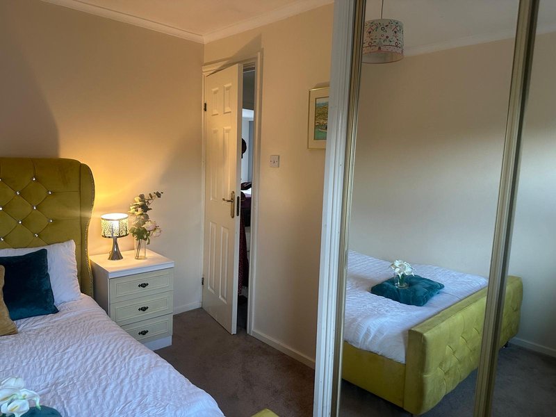 Bedroom with double bed, green upholstered headboard, bedside table and mirror wardrobe